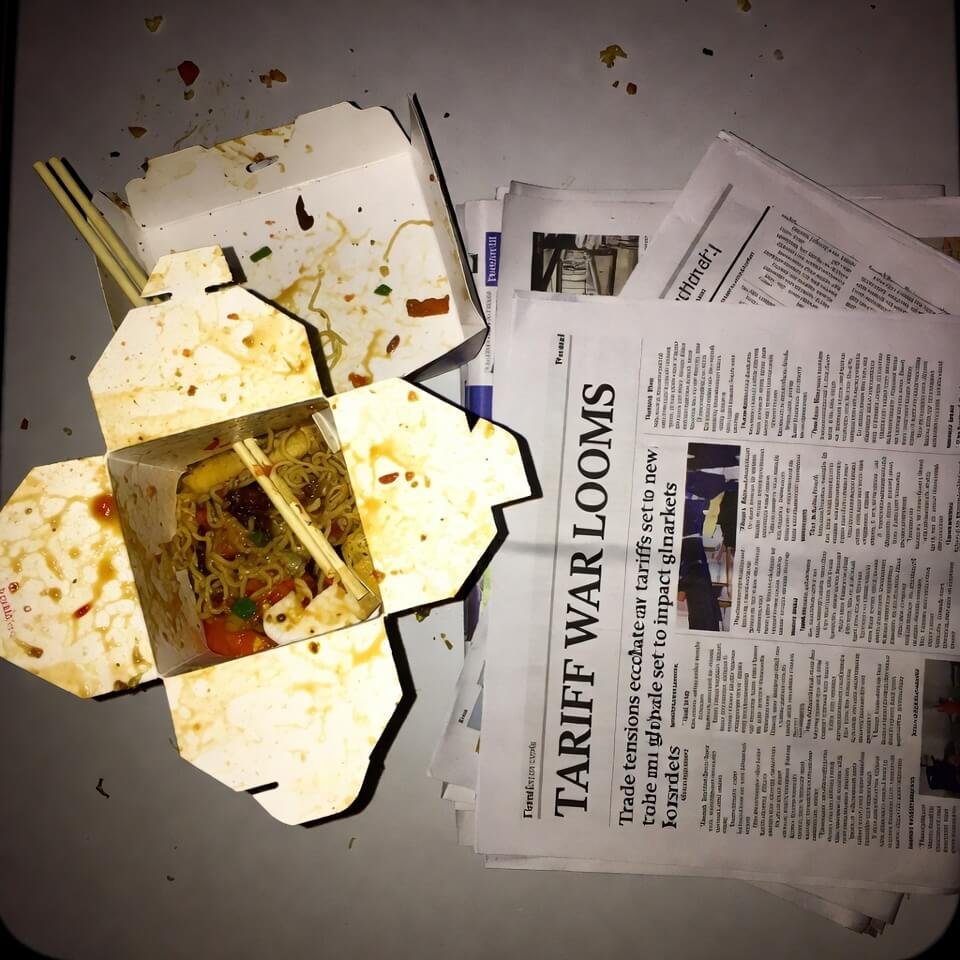 Half-eaten Chinese takeout container amid crumbs and tariff news articles.