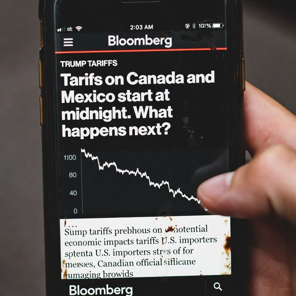 Tilted phone screen showing Bloomberg tariff news at 2 a.m. with coffee stains.